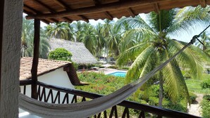 A hammock on a balcony overlooking a pool and palm trees. - Casa Don Pepe (Barra de Potosi)