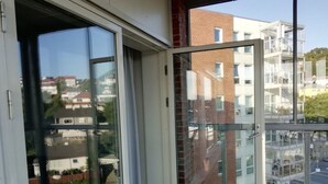 A modern apartment with a glass door leading to a balcony, a wooden floor, and a view of neighboring buildings. - Gauk Apartments Sentrum 3 (Sandnes)
