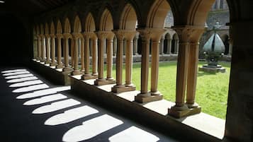 Stroll through the beautifully designed corridor, lined with arches and columns, leading to a serene courtyard with a grassy area and a statue.