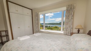 A bedroom with a large bed, a wardrobe, and a window with a view of a lake and hills. - Peaceful Farm Cottage in the 'Heart of Argyll' over-looking Loch Awe (Dalmally)