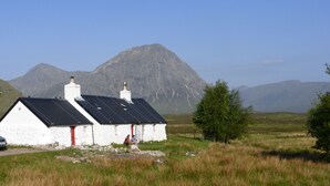 A white building with a black roof and red door, surrounded by grass and mountains. - Peaceful Farm Cottage in the 'Heart of Argyll' over-looking Loch Awe (Dalmally)