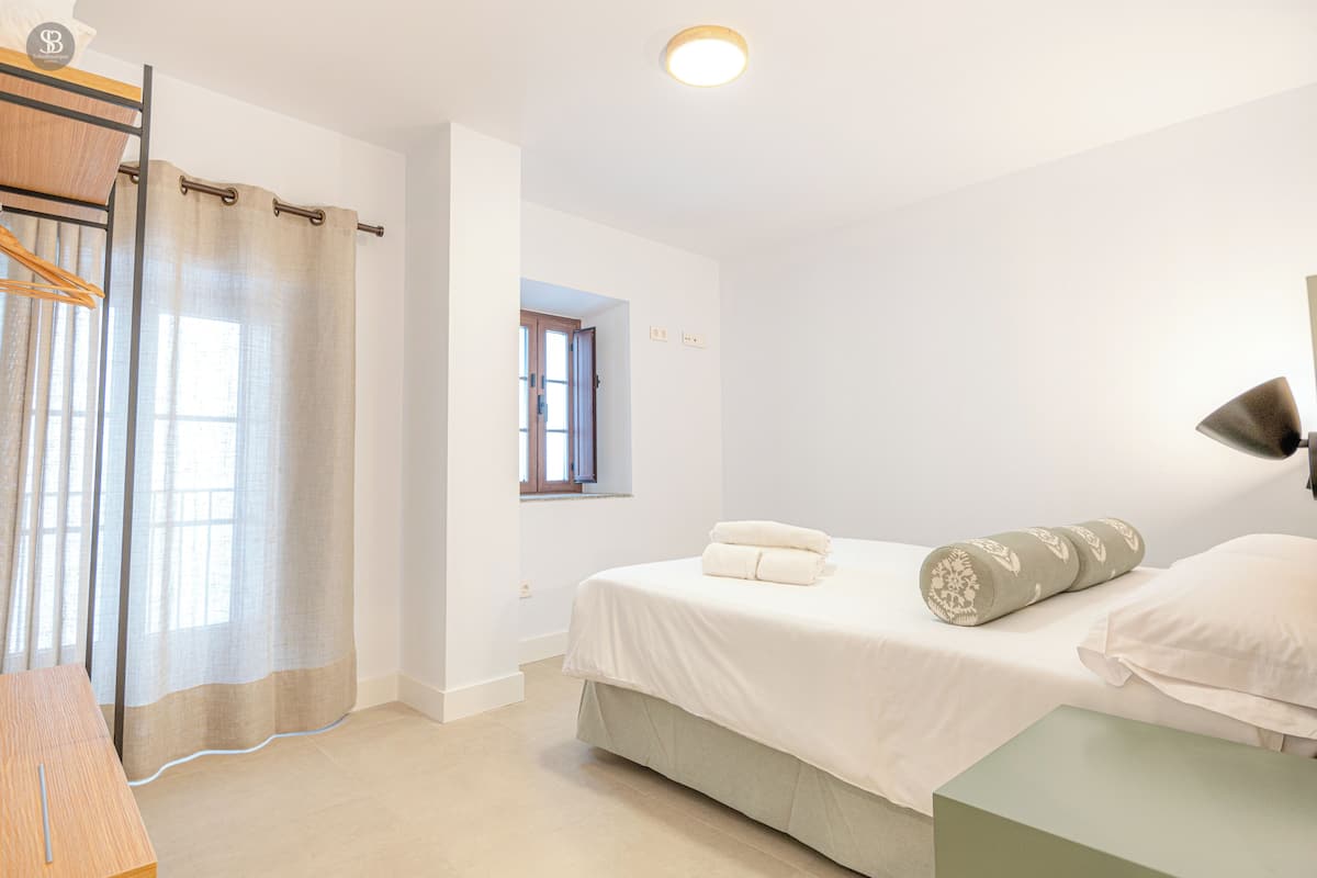A bedroom with a bed, a bedside table, a window, and a door.