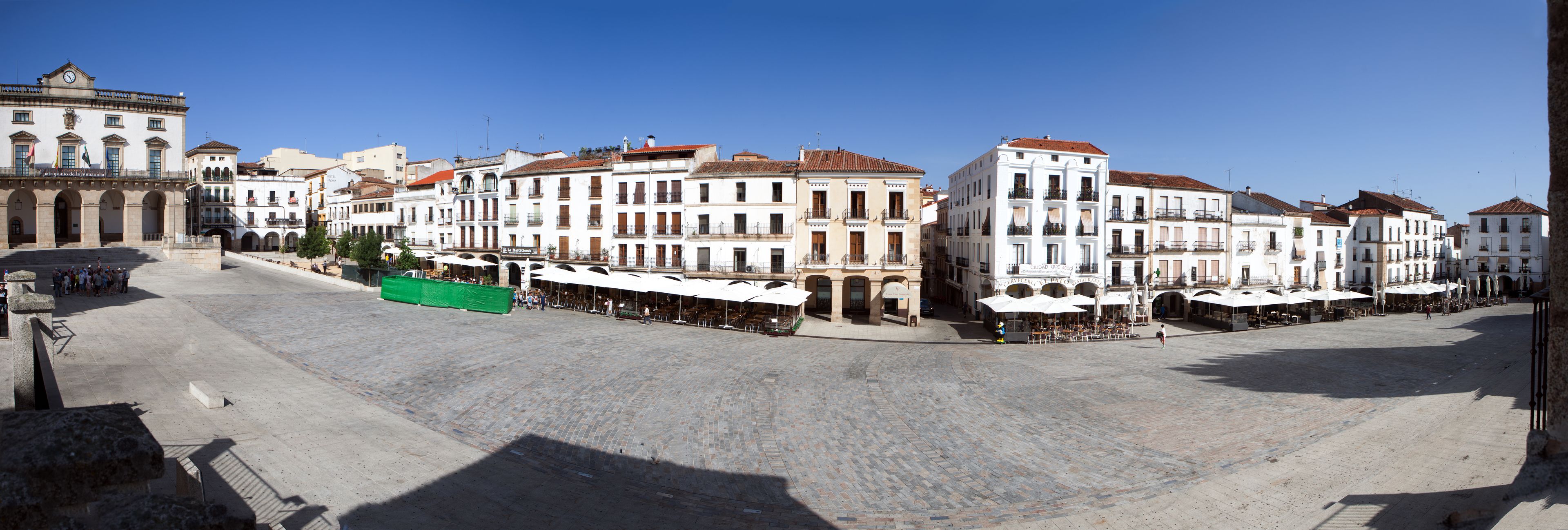 Una plaza con edificios históricos, mesas al aire libre y un amplio espacio abierto.