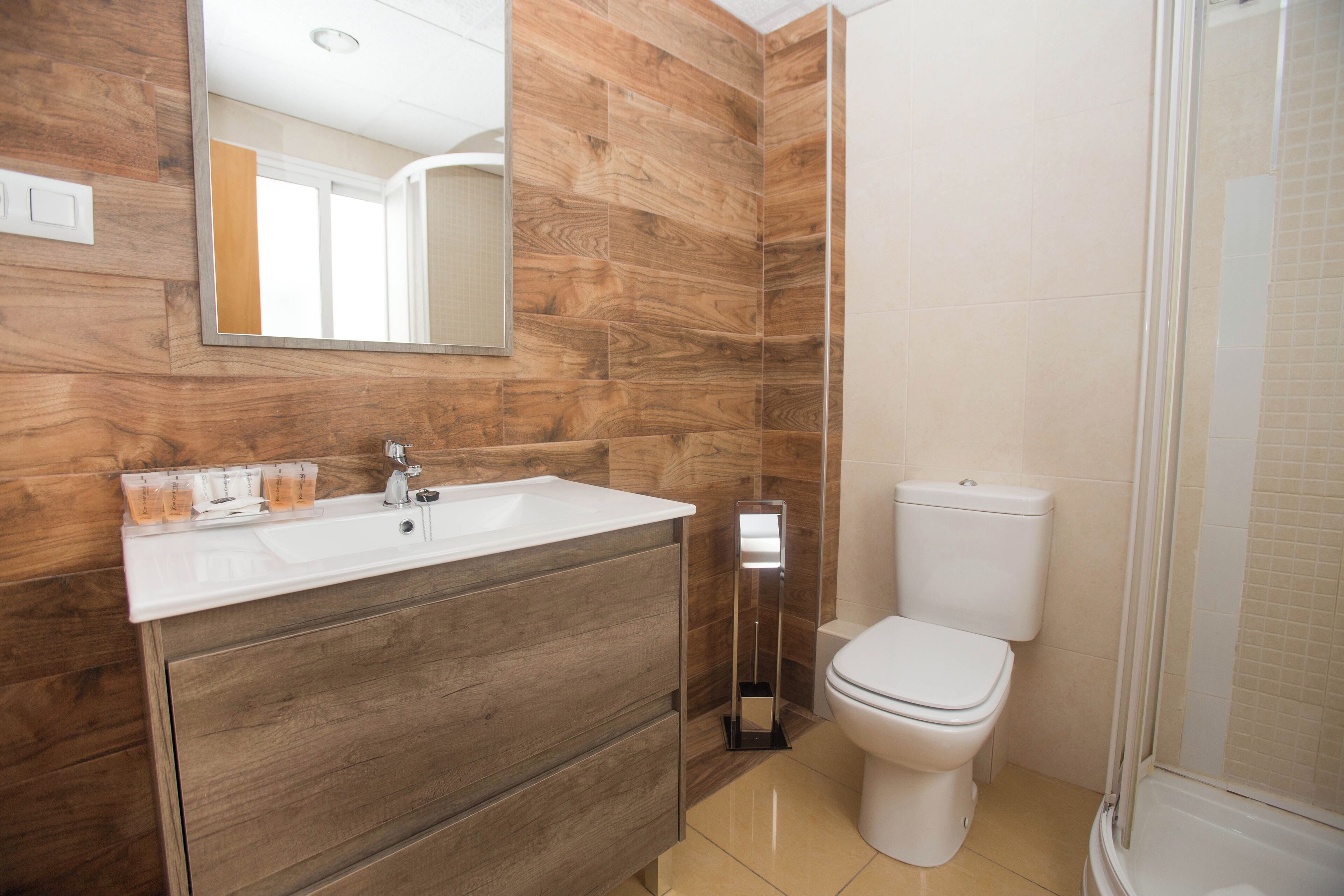 A bathroom with a wooden vanity, a white sink, a toilet, and a glass shower enclosure.
