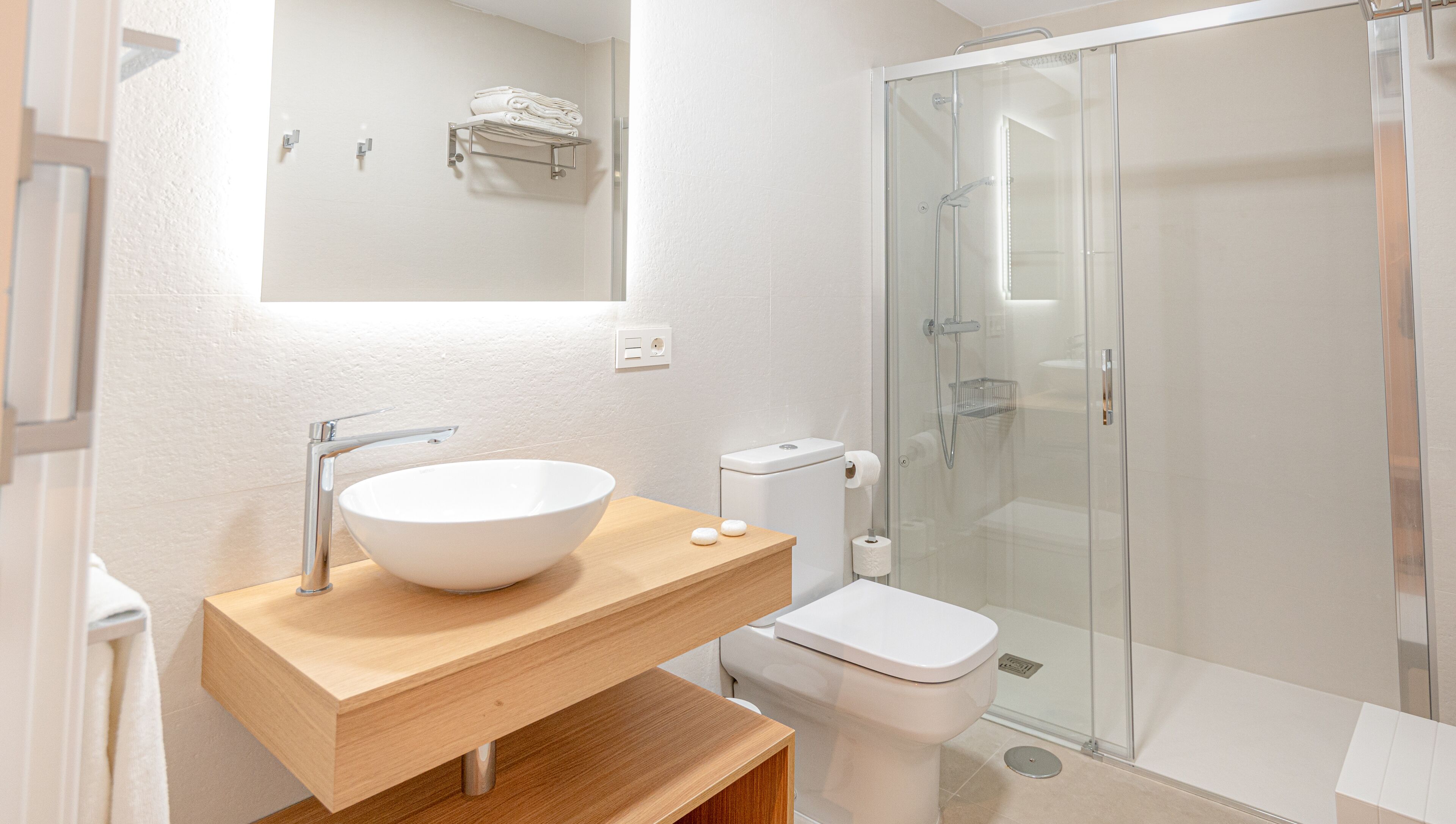 Un baño moderno con un lavamanos grande blanco, un inodoro y una ducha con mampara de vidrio.