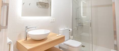 Un baño moderno con un lavamanos grande blanco, un inodoro y una ducha con mampara de vidrio.
