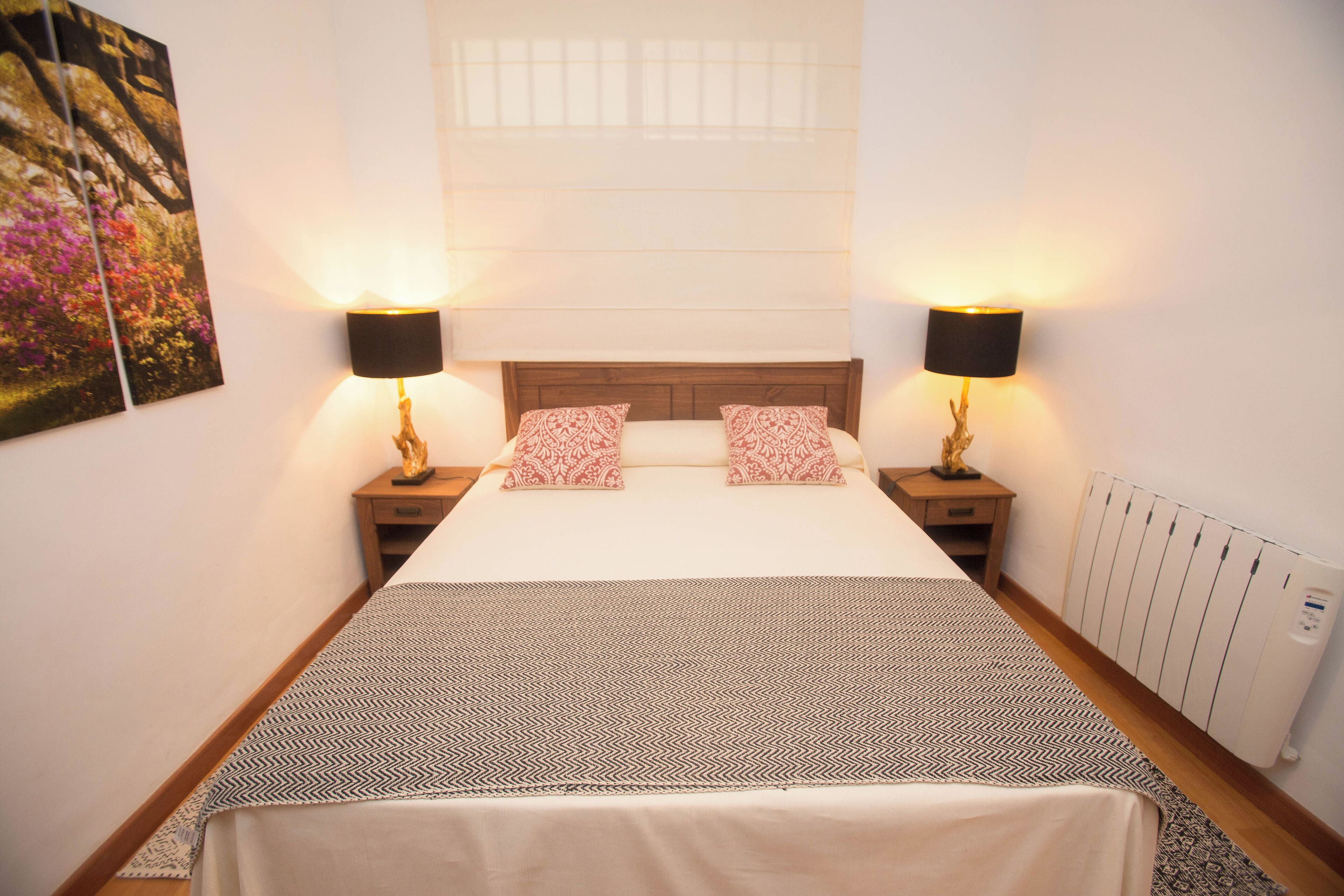 A neatly made bed with a patterned bedspread, two bedside lamps, and a nightstand with a decorative item.