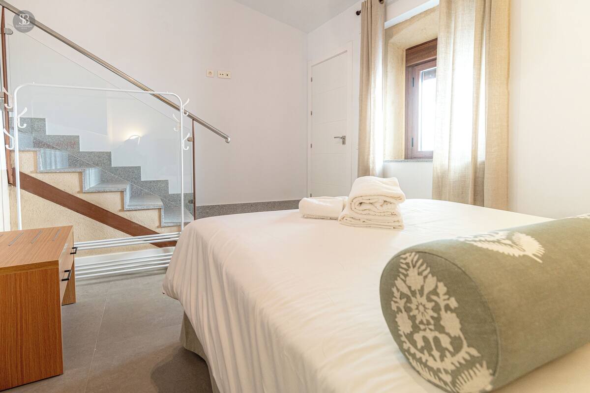 A hotel room with a bed, a wooden desk, a glass railing, and a staircase.