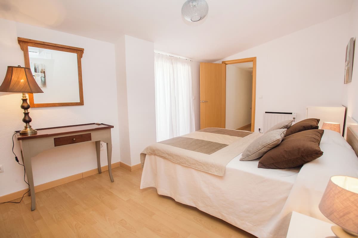 A bedroom with a bed, bedside table, lamp, and a mirror on the wall.