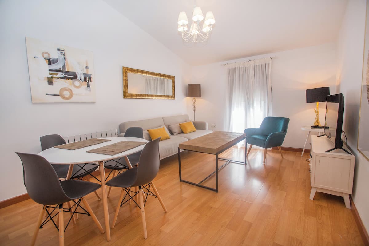 A modern living room with a dining table, chairs, a sofa, a TV, and artwork on the walls.