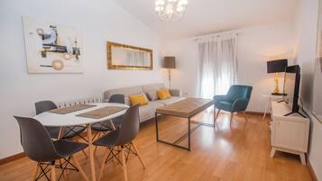 Una sala de estar moderna con una mesa de comedor, sillas, un sofá, un televisor y obras de arte en las paredes.