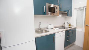 Una cocina compacta con armarios verde azulado, un microondas de acero inoxidable, un lavavajillas y un fregadero.