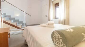 Habitación de hotel con una cama, un escritorio de madera, una barandilla de cristal y una escalera.