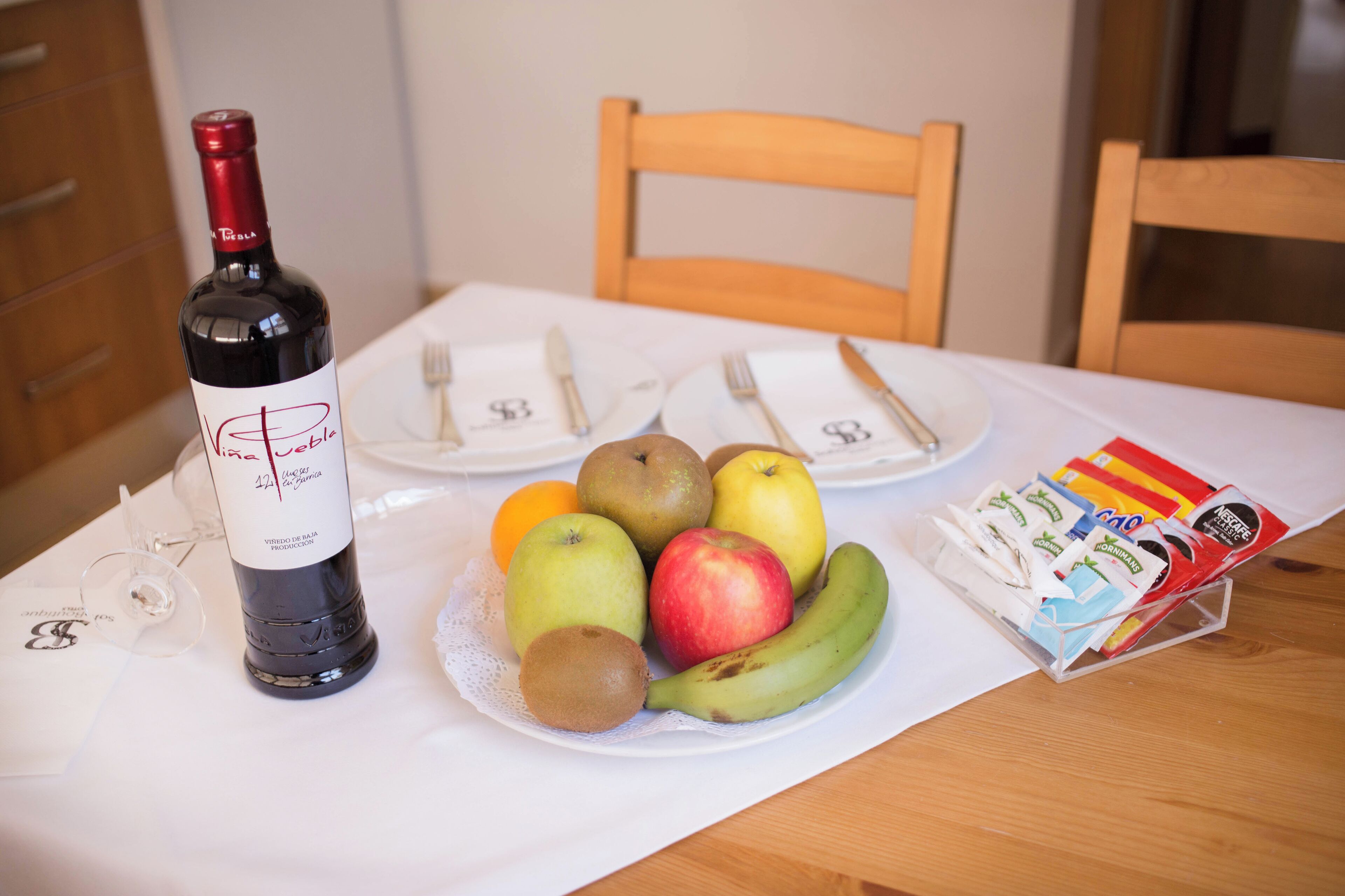 Una mesa con una botella de vino, platos de fruta y una cesta de aperitivos.