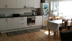 A modern kitchen with white cabinets, a built-in oven, and a refrigerator. There is a dining area with a table and chairs. - Pulpit Rock Family Apartment (Sandnes)