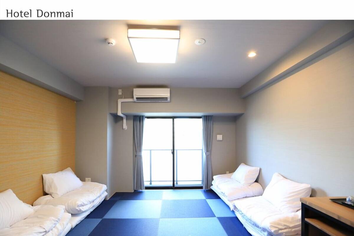 A hotel room with two beds, a large window, and a ceiling fan.