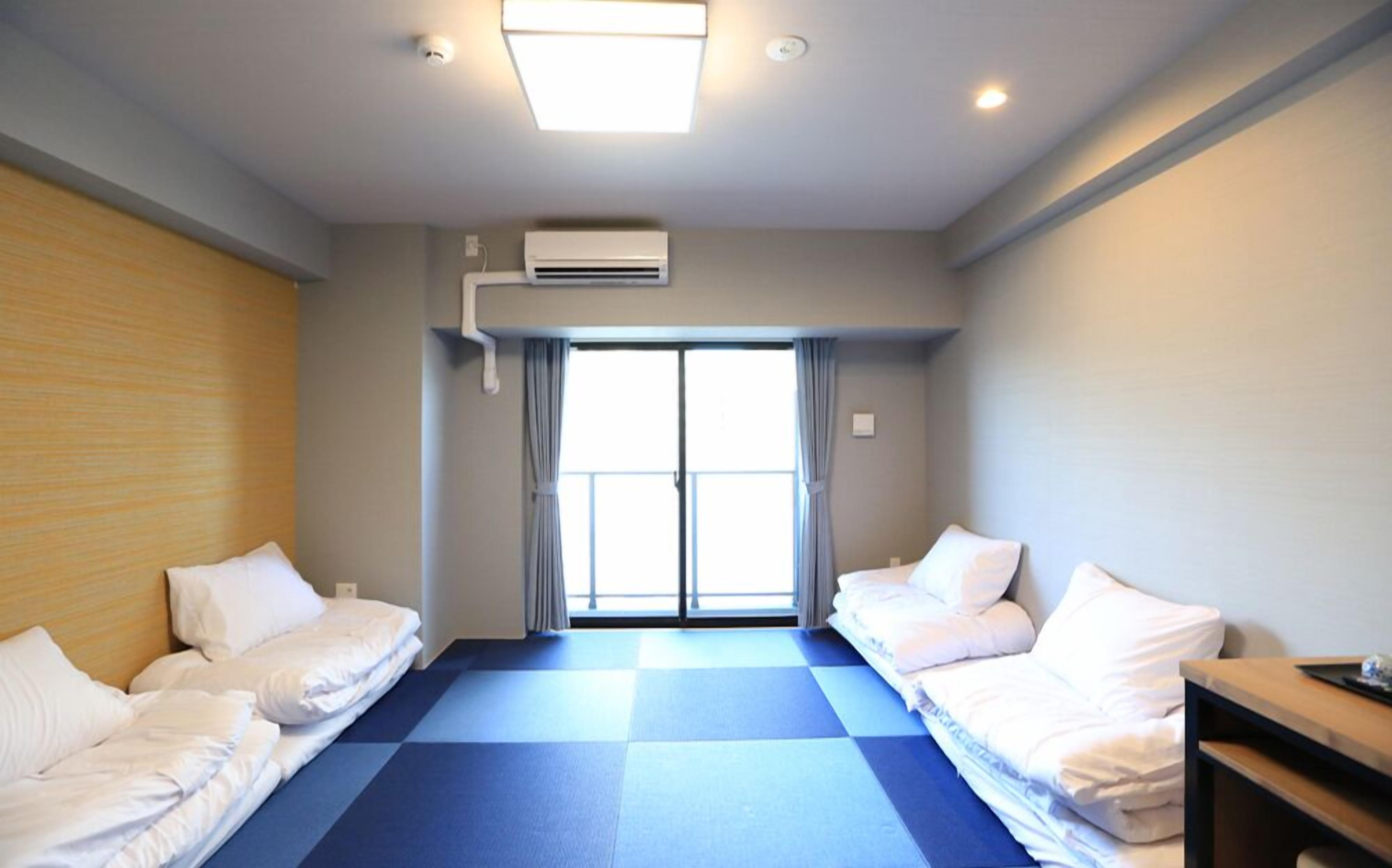 Una habitación de hotel con dos camas, un ventanal grande, un equipo de aire acondicionado y un suelo a cuadros.