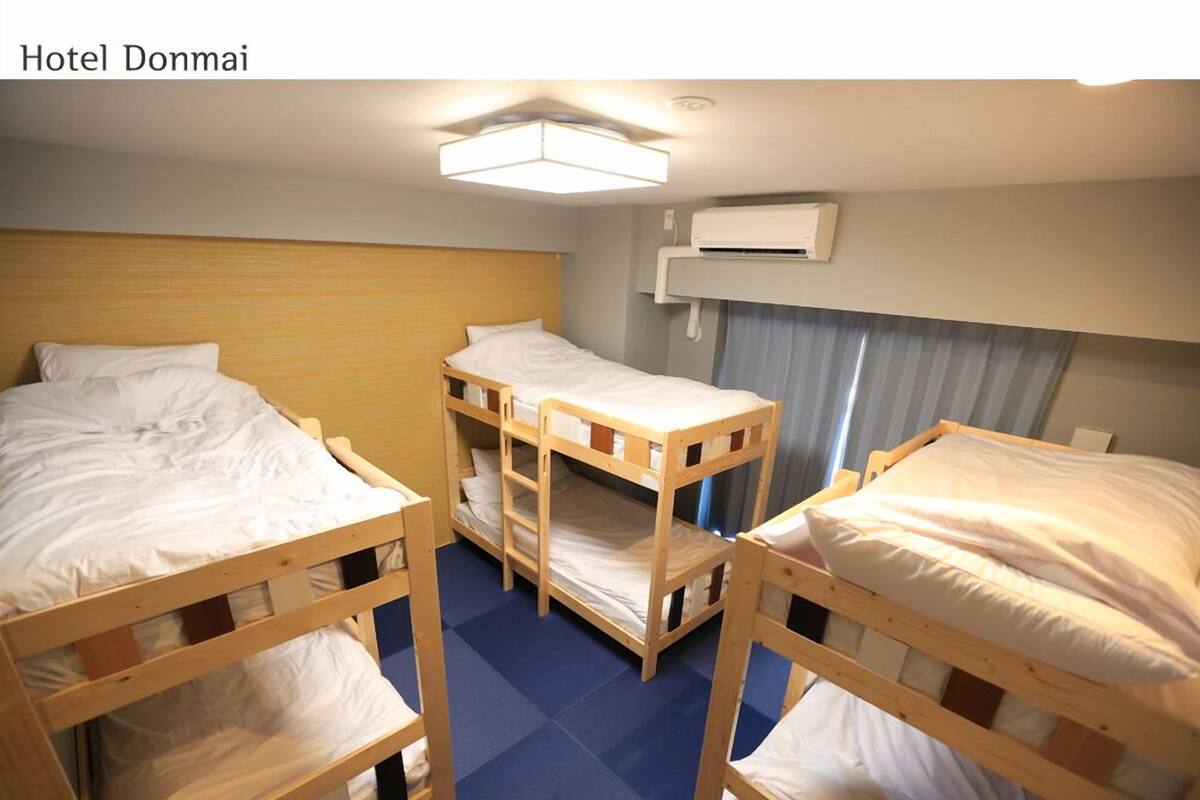 A hotel room with three bunk beds, a ceiling light, and an air conditioning unit.