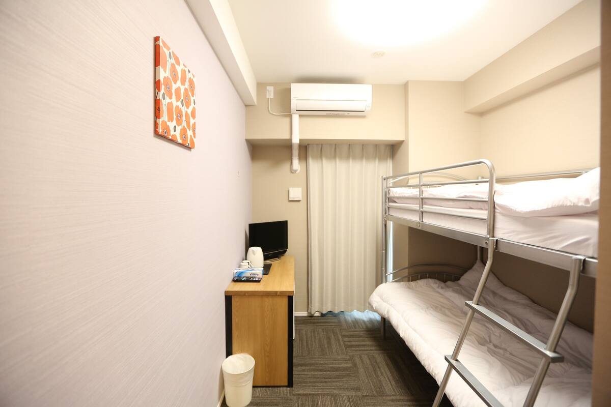A compact hotel room with bunk beds, a desk with a computer, and an air conditioning unit.