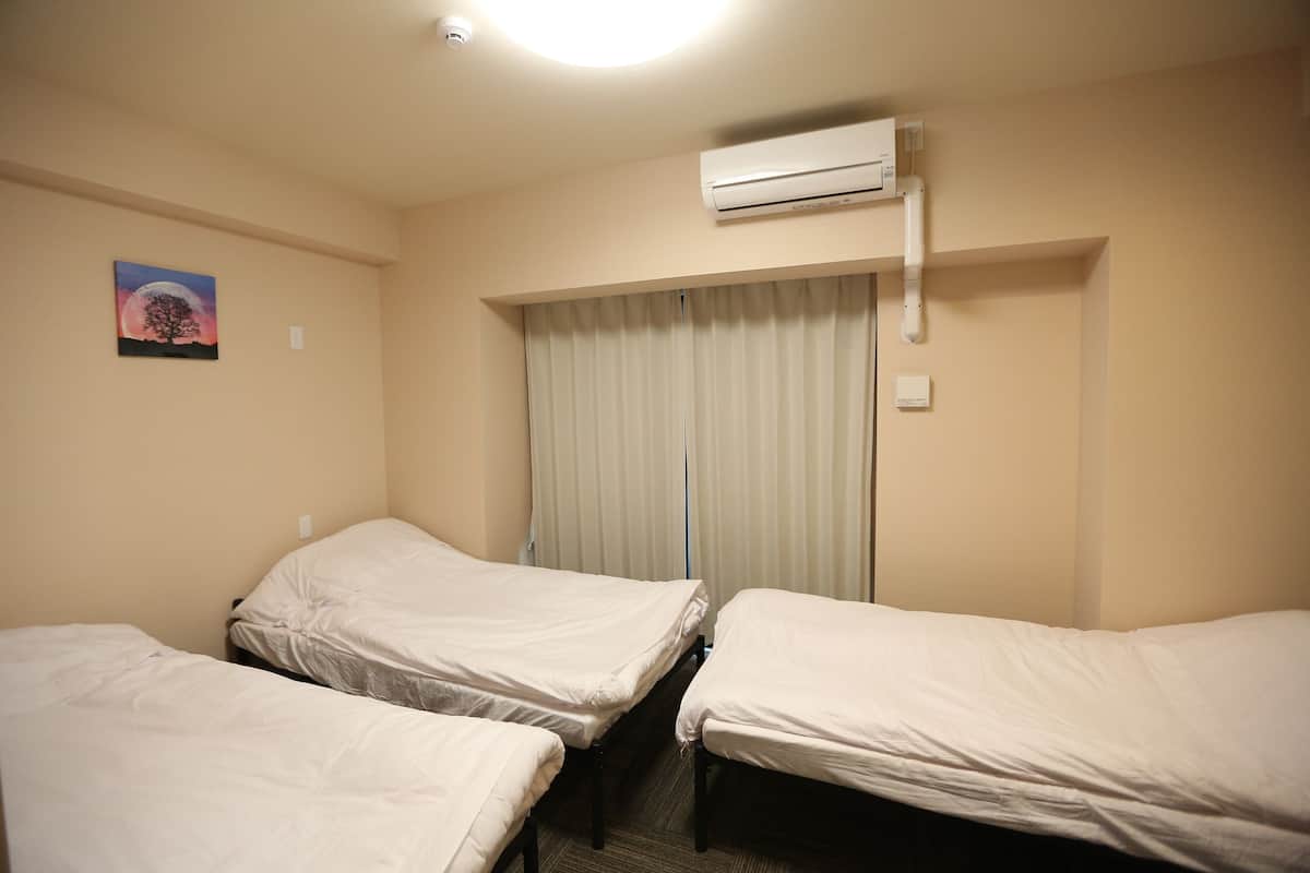 A hotel room with two single beds, a large window with curtains, an air conditioning unit, and a wall-mounted painting.