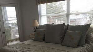 A bedroom with a bed, a nightstand, a lamp, and a window with blinds. - Eagle Cay Condo (Marco Island)