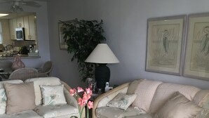A living room with a sofa set, a glass coffee table with flowers, a lamp, and framed artwork on the wall. - Eagle Cay Condo (Marco Island)