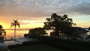 A sunset view over a body of water with a palm tree and a building in the foreground. - Eagle Cay Condo (Marco Island)