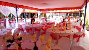 Un événement en plein air se déroulant sous des tentes, avec des tables rondes, des nappes blanches et des rubans rouges.