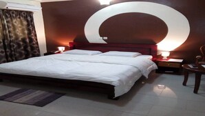 Une chambre d’hôtel avec un grand lit, deux tables de chevet avec des lampes, une petite table en bois, une chaise et un grand élément décoratif mural.