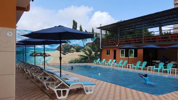 Un espace piscine avec des chaises longues et des parasols, une fresque représentant une scène de plage et un espace de repos abrité.