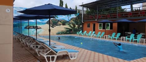 Una piscina al aire libre, sombrillas, sillones reclinables de piscina