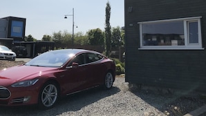 Ein rotes Auto vor einem Gebäude mit einer Fassade in Grün und Grau, ein Fenster mit der Nummer 155 und eine Schotterauffahrt.