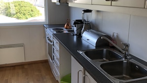 Eine moderne Küche mit weißen Schränken, einer schwarzen Arbeitsplatte und Edelstahlgeräten, darunter ein Wasserkocher, ein Mixer und eine Spüle.