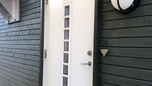 Eine weiße Tür mit Fenster, einem Zahlenschloss und einer Lampe an einer dunkelholzigen Wand.