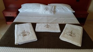 Ein ordentlich bezogenes Bett mit weißen Leinen und Kissen, ein Holzkopfbrett und ein brauner Nachttisch mit einer Schublade.