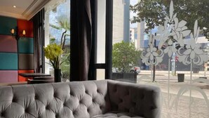 A grey tufted sofa in a modern hotel room with large windows, a view of the street, and a decorative metal plant sculpture. - Hôtel Europole (Grenoble)