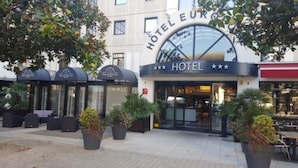A hotel entrance with a large sign, potted plants, and outdoor seating. - Hôtel Europole (Grenoble)