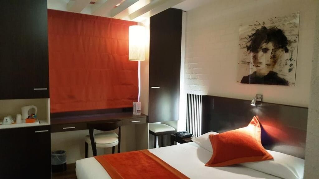 A hotel room with a bed, a desk, a chair, and a lamp.