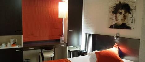 A hotel room with a bed, a desk, a chair, and a lamp.