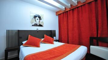 A hotel room with a bed, a nightstand, a chair, a red curtain, and a painting on the wall.