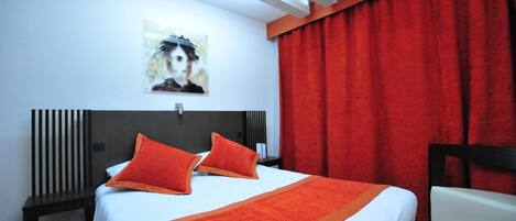 A hotel room with a bed, a nightstand, a chair, a red curtain, and a painting on the wall.