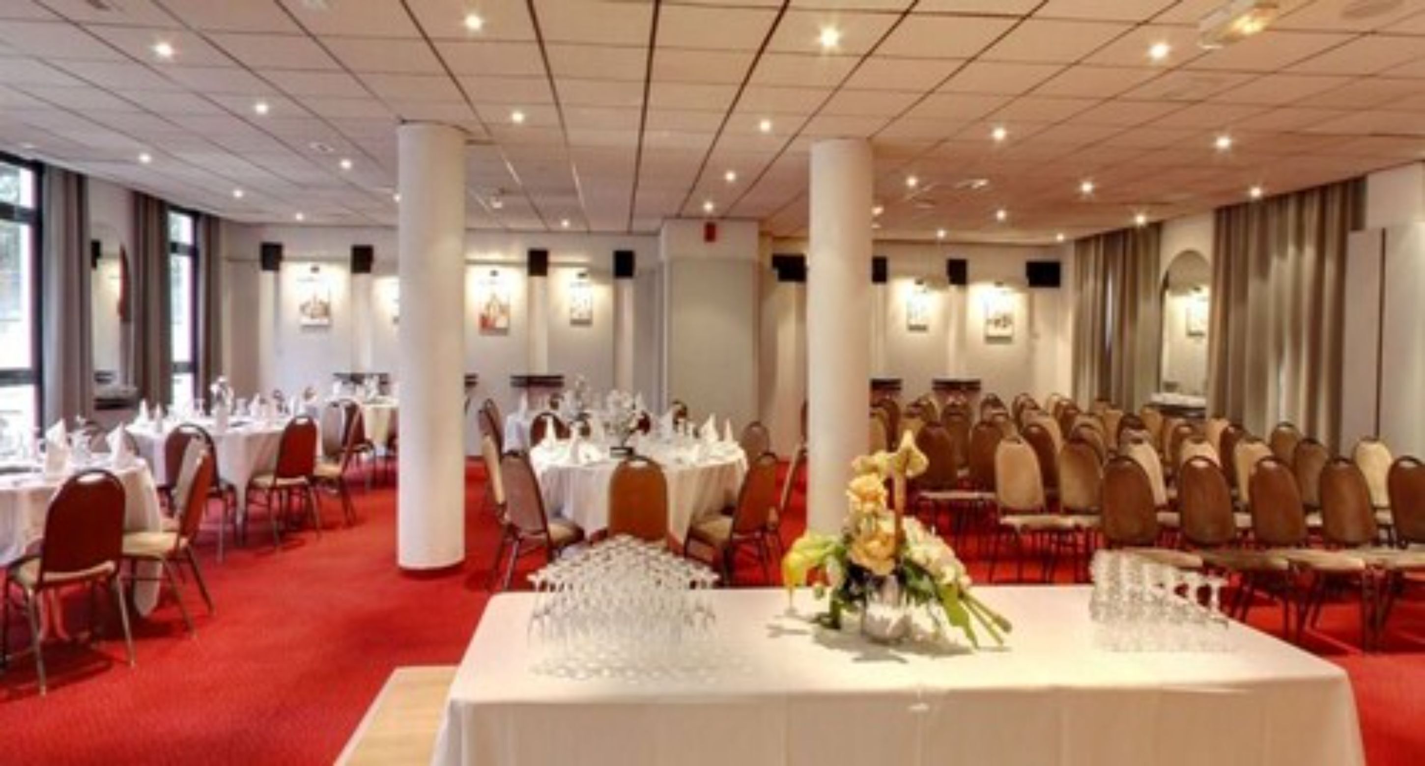 Un salón de banquetes con mesas redondas dispuestas para comer, manteles blancos y sillas.