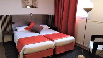Habitación de hotel con cama doble, cabecera, mesita de noche, lámpara de pie y un cuadro en la pared.