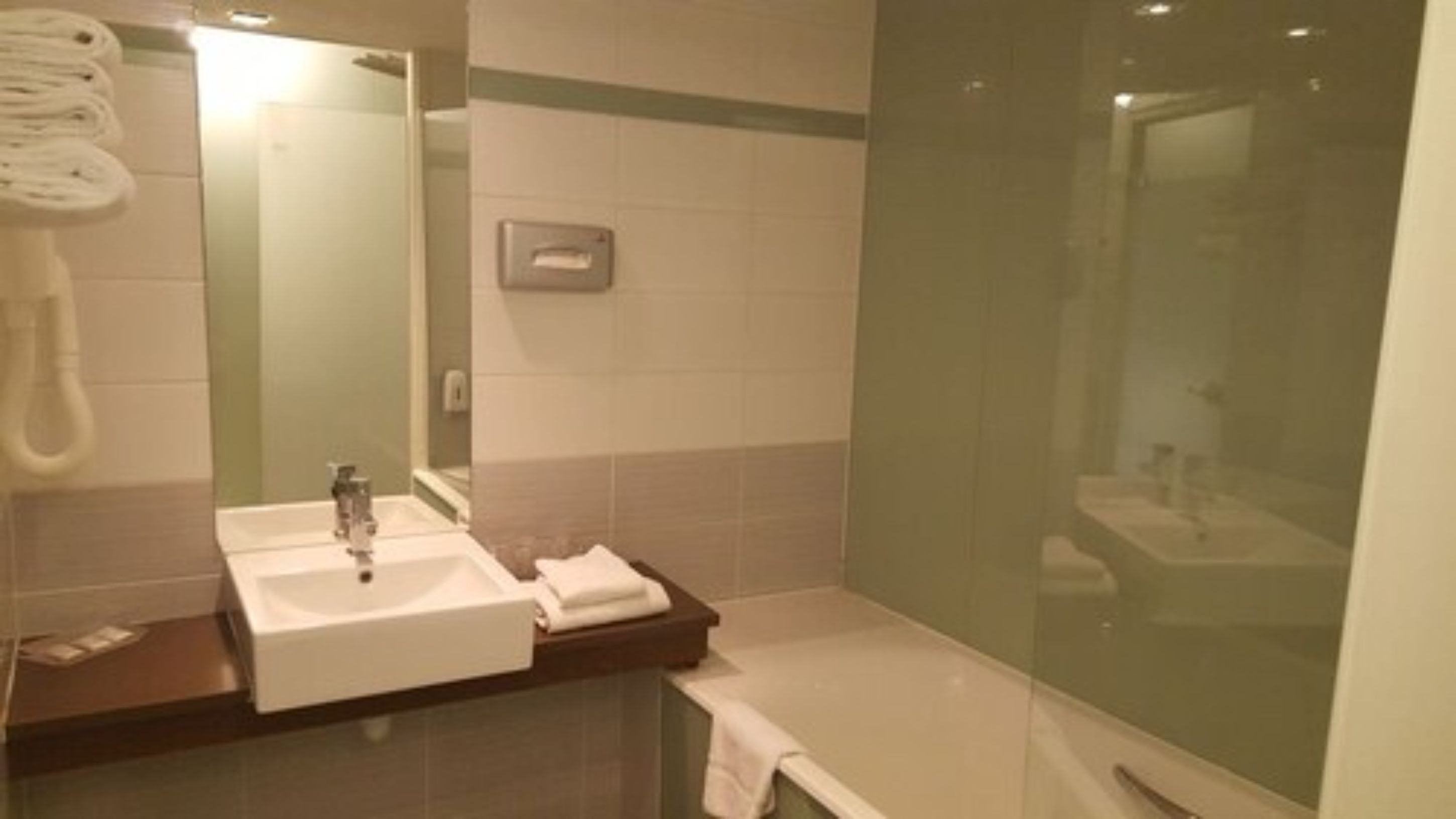 Un baño con lavamanos, espejo, toallero y zona de ducha.
