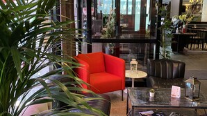 A modern lobby with a red armchair, a tufted sofa, and a glass coffee table with magazines. - Hôtel Europole (Grenoble)