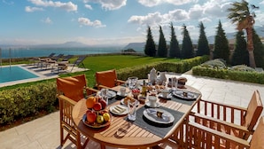 A dining table set with breakfast items and a view of a swimming pool and mountains. - Ocean Villas Complex by Ocean Residences (Malevizi)