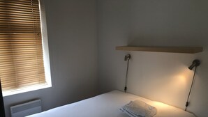 A single bed with a folded towel, a wall-mounted shelf, and two wall-mounted lamps. - Gauk Apartments Sentrum 4 (Sandnes)