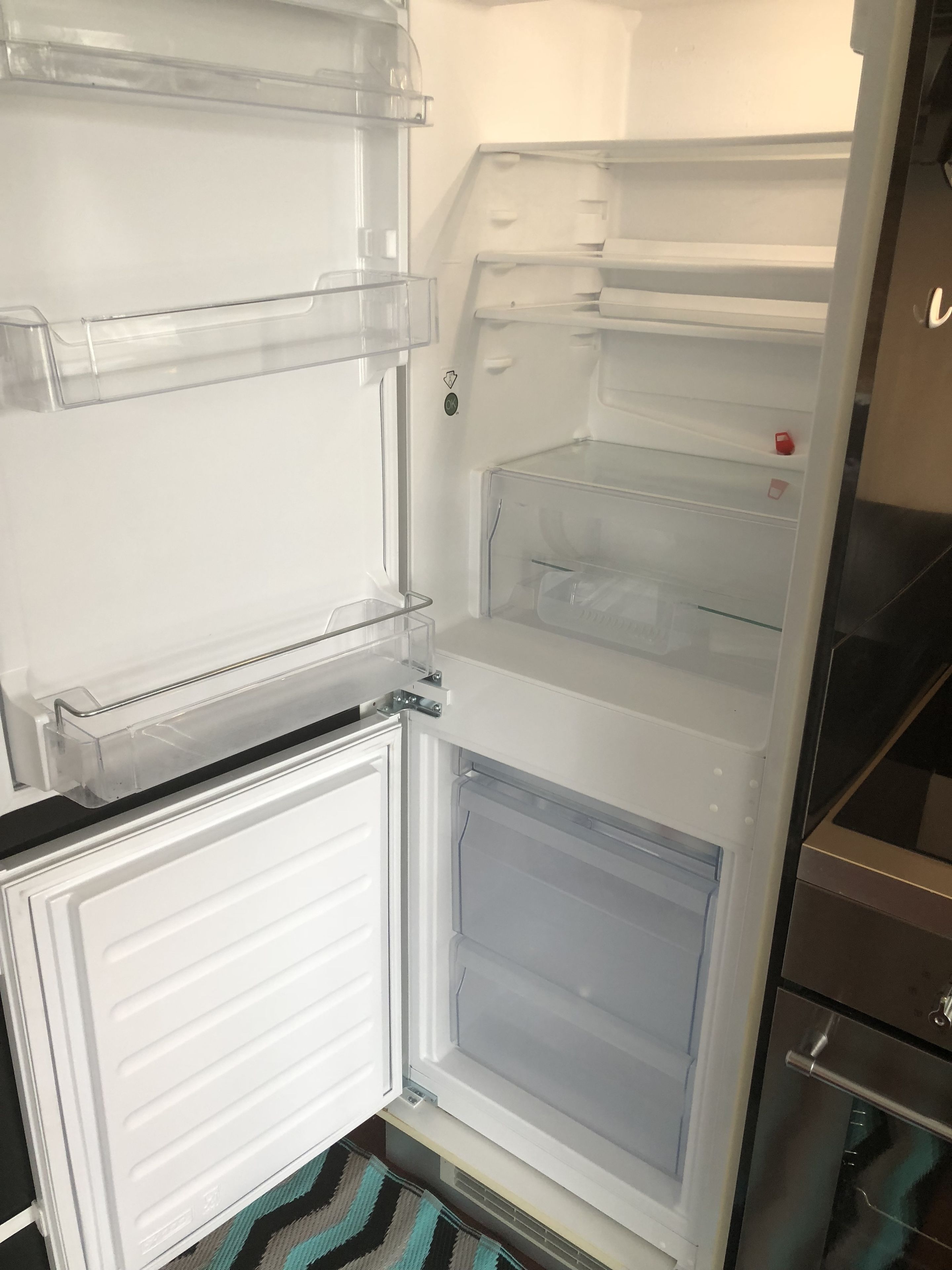 Een open koelkast met transparante planken en een vriesvak.
