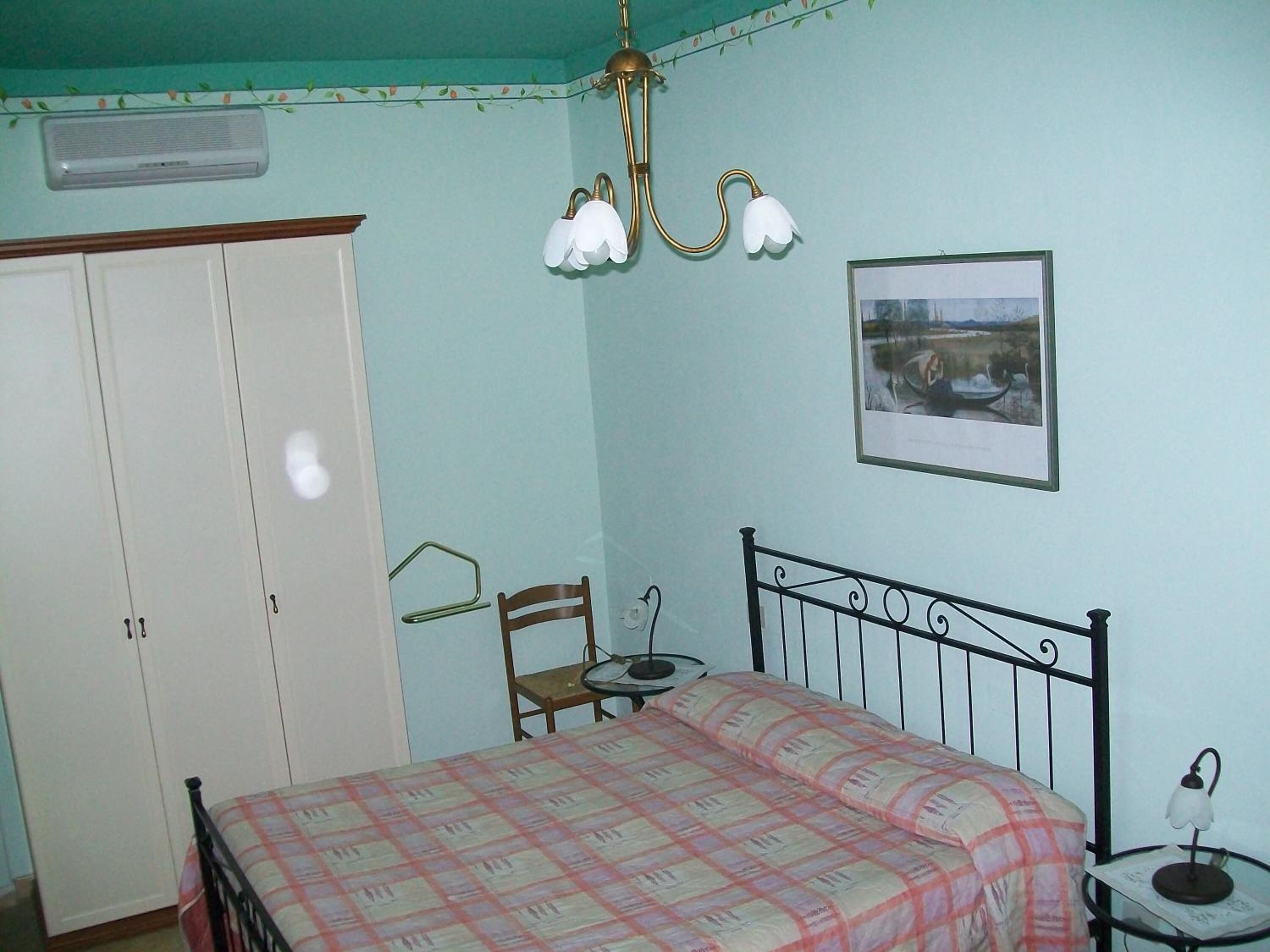 Ein Schlafzimmer mit Bett, Kleiderschrank, Stuhl, Tisch, Lampe und einem Bild an der Wand.