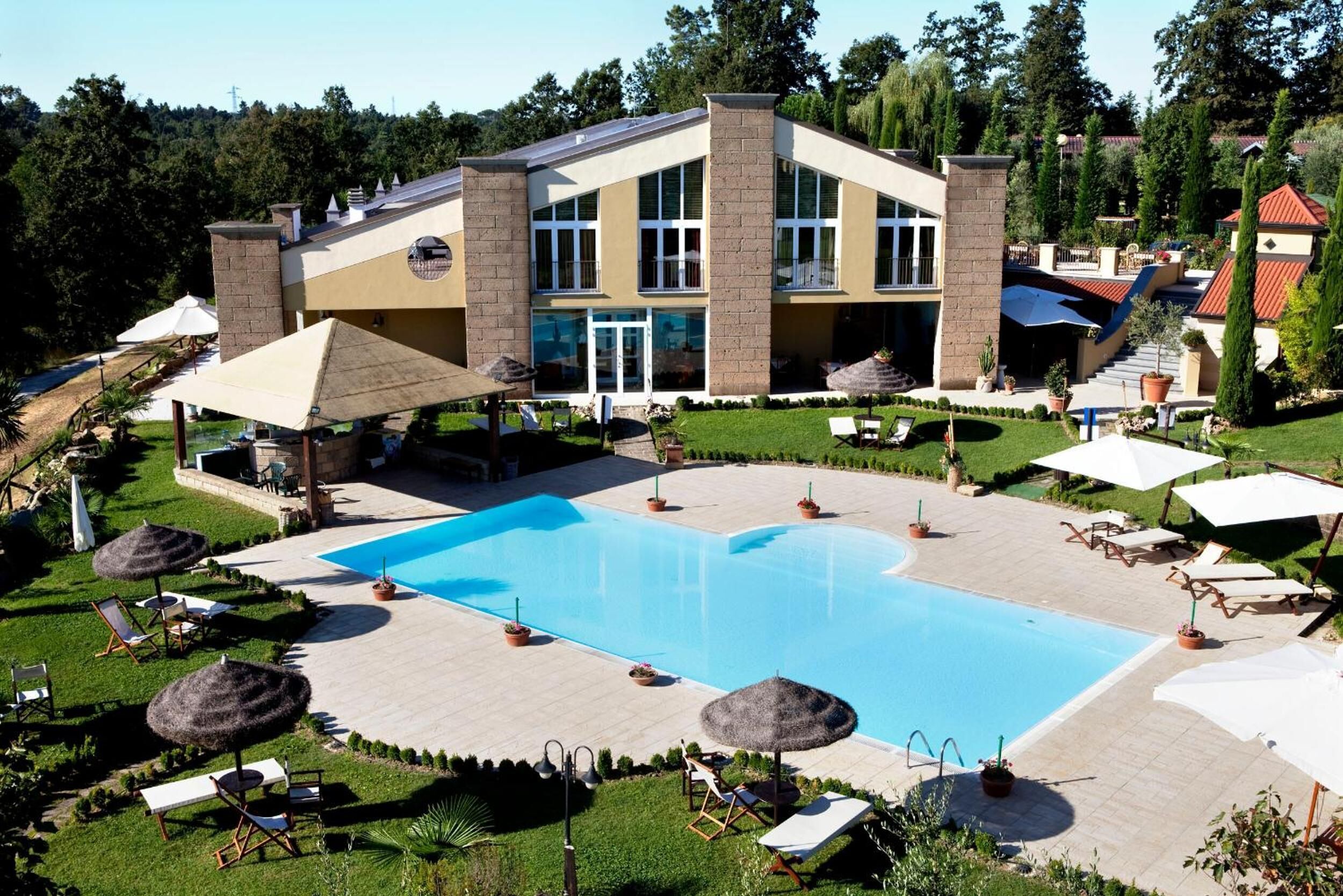 A modern hotel with a swimming pool, sun loungers, and umbrellas.